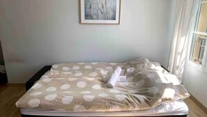 Un letto rifatto con una coperta a motivi, un asciugamano arrotolato e un quadro appeso al muro.