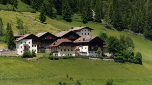 Un ensemble de bâtiments de style chalet traditionnel, à plusieurs étages et dotés de balcons, entouré de prairies verdoyantes et d’une forêt dense.