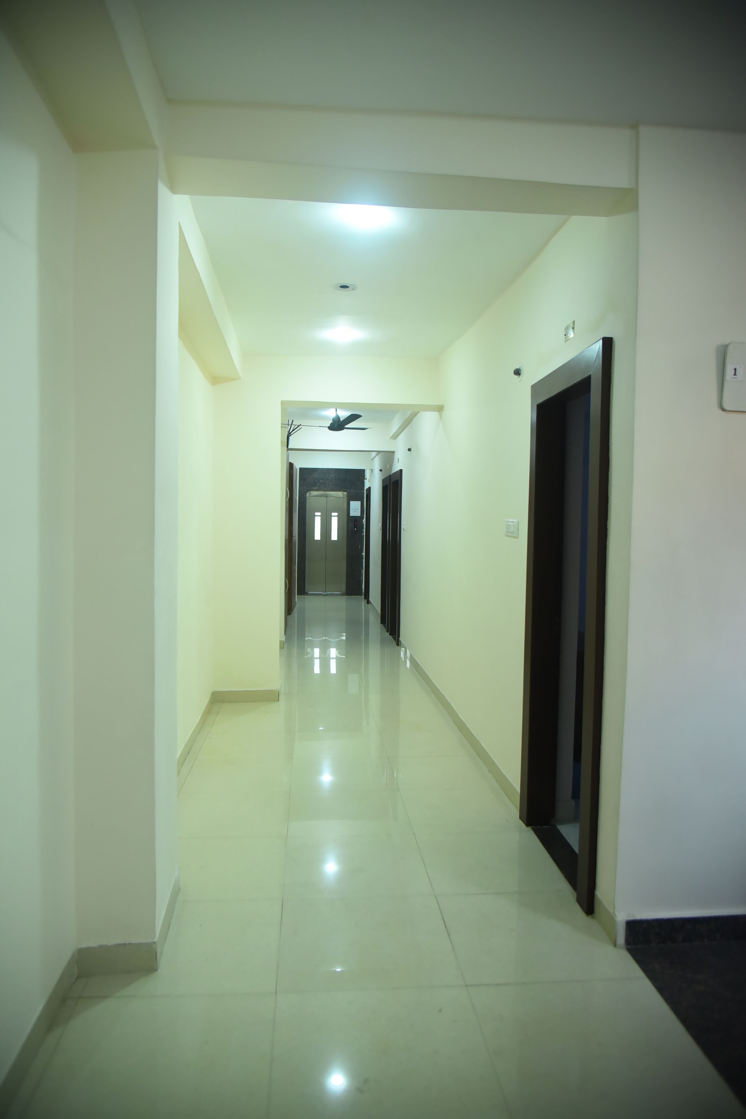 A long, narrow hallway with a shiny floor, doors on both sides, and a ceiling light.