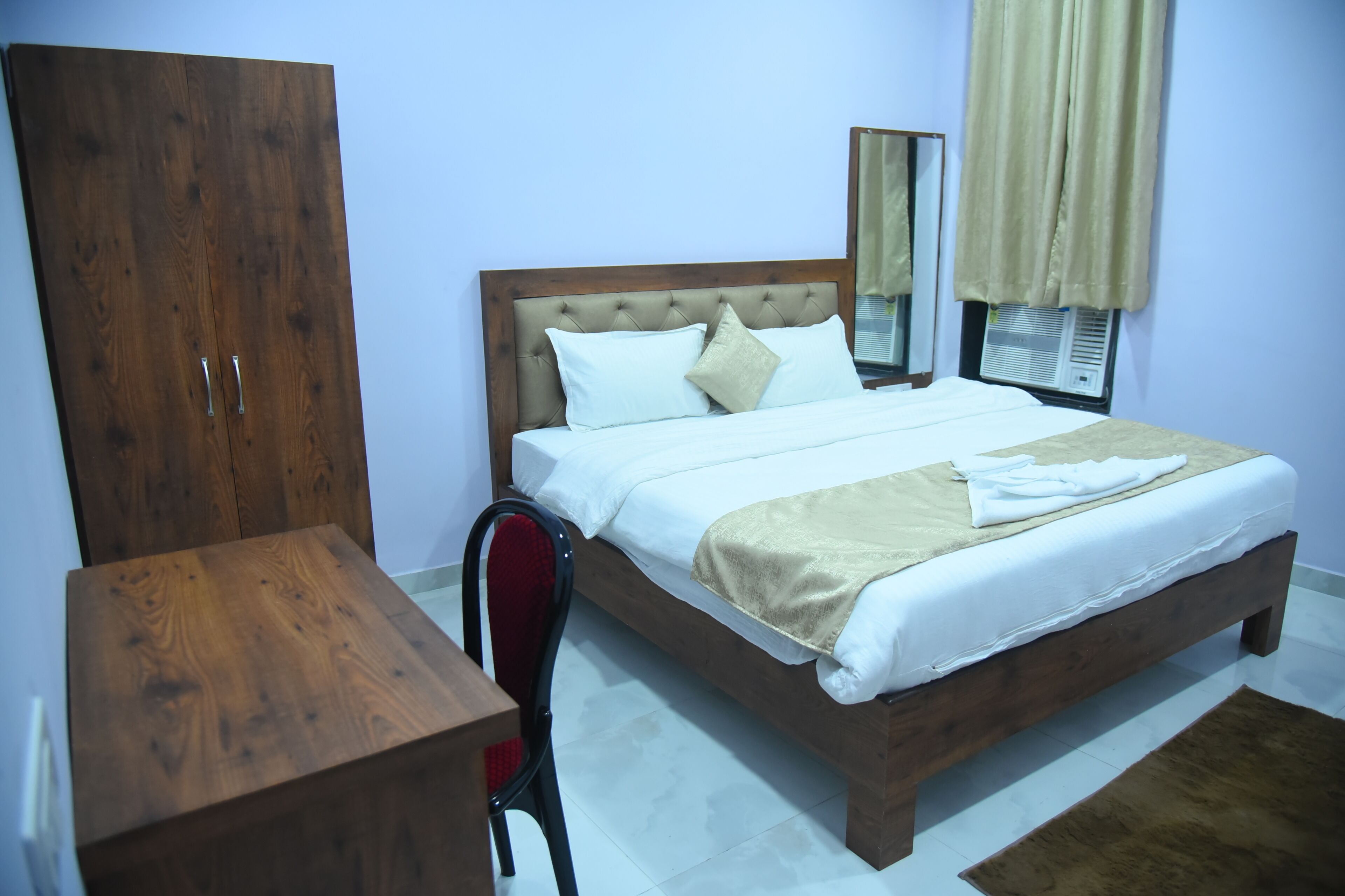 Un dormitorio con una cama de madera, ropa de cama blanca, un armario de madera, una silla y un espejo en la pared.