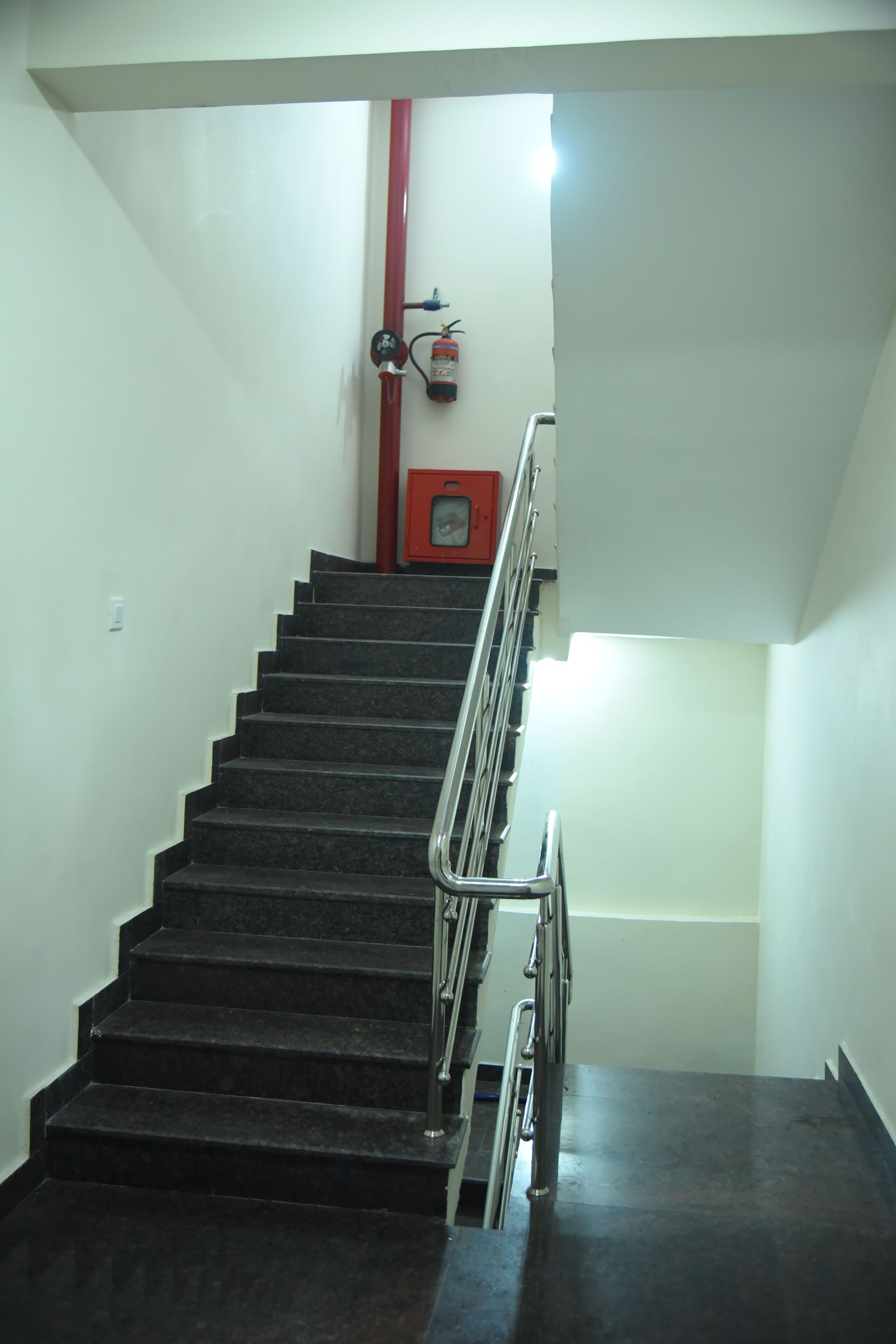 Een trap met een metalen leuning, een brandblusser aan de muur en een rode noodtelefoon.