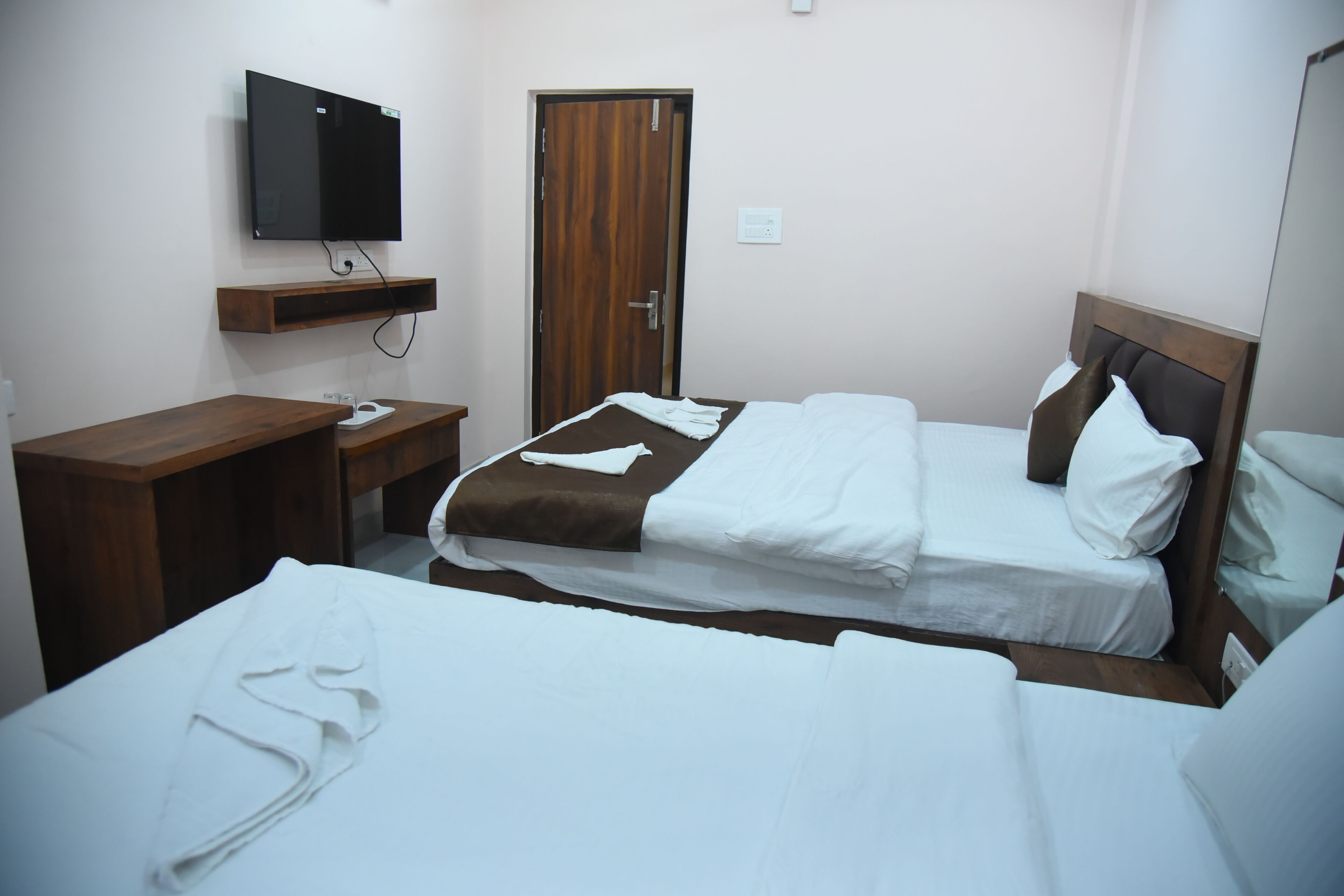 Une chambre d’hôtel avec deux lits, un téléviseur fixé au mur, un bureau en bois et une armoire.
