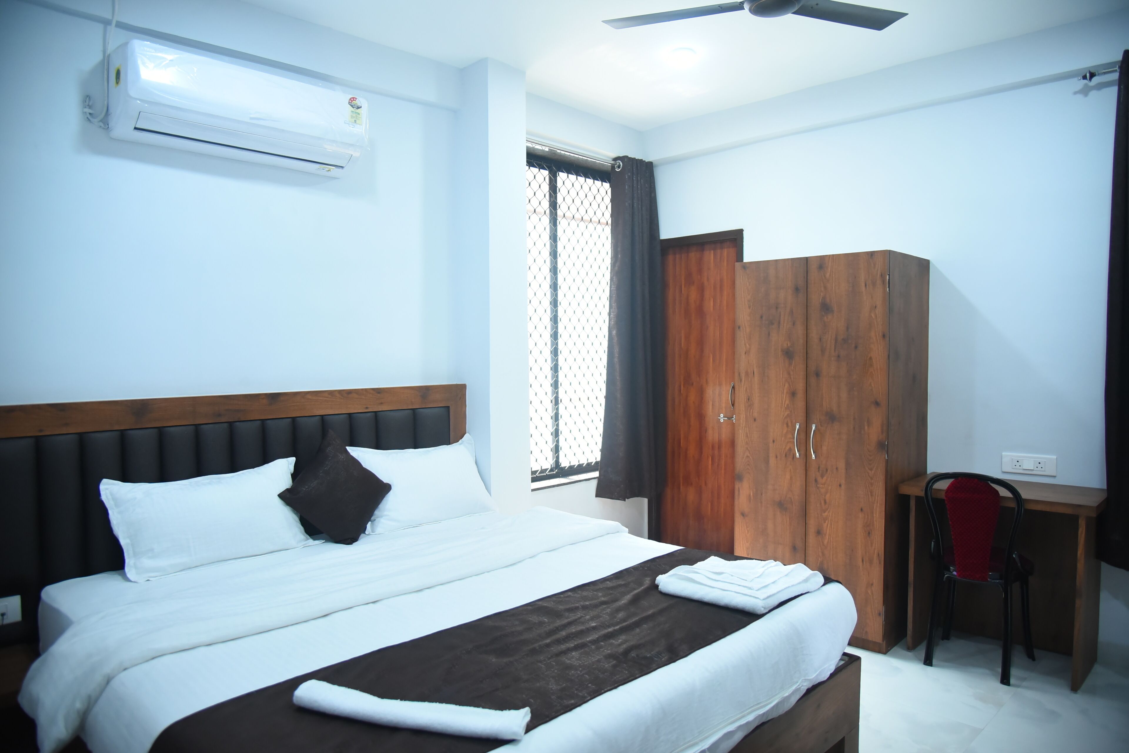 Una habitación de hotel con cama, escritorio, armario y aire acondicionado.
