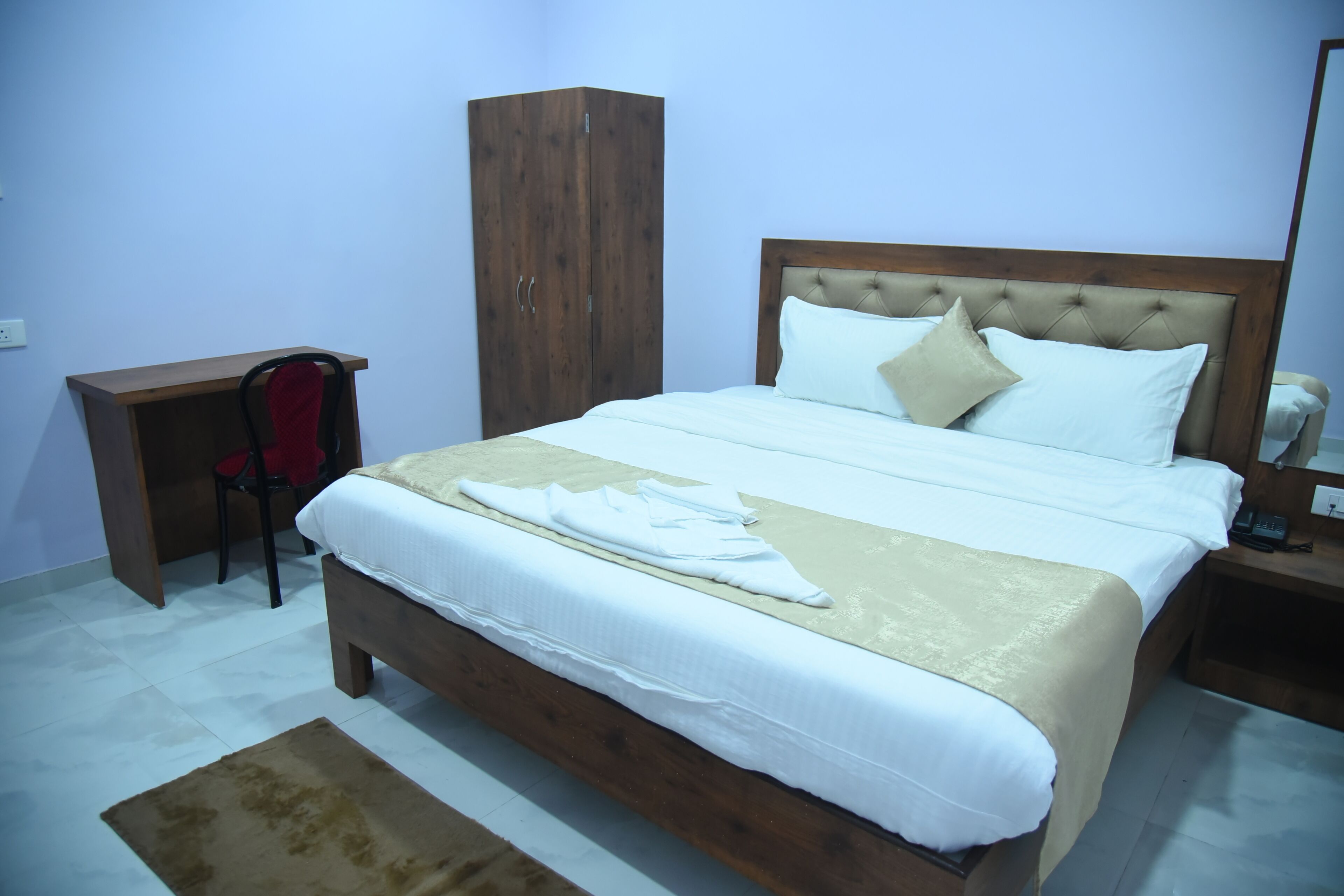 A neatly made bed with a wooden headboard, a bedside table with a lamp, and a chair.