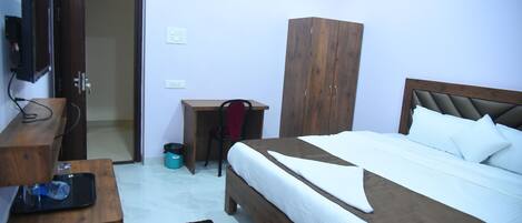 Une chambre à coucher comprenant un lit, une armoire en bois, un bureau et un téléviseur posé sur un meuble.