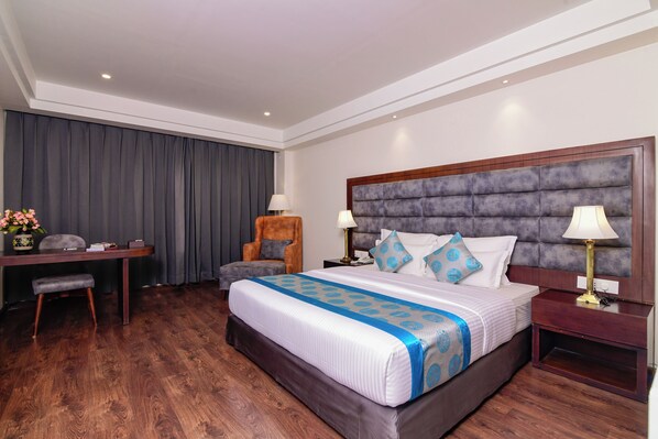 Habitación de hotel con una cama grande, un escritorio, una silla y una mesita de noche con lámparas.