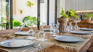 A dining table set with plates, cutlery, and glassware, surrounded by chairs and potted plants.