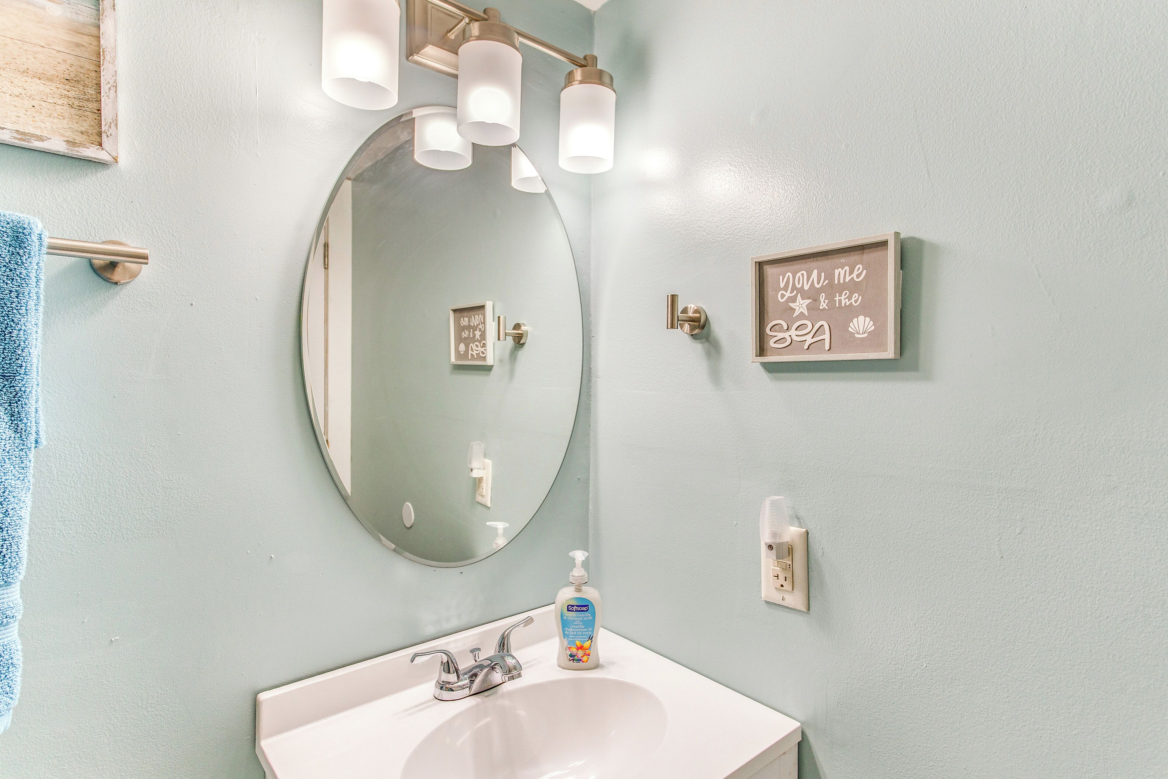 A bathroom with a round mirror, a white sink, and a soap dispenser.