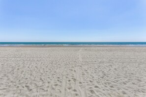 A wide sandy beach with visible footprints and a clear blue sky.