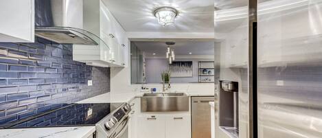 A modern kitchen with white cabinets, a stainless steel range hood, a built-in oven, a dishwasher, and a refrigerator.