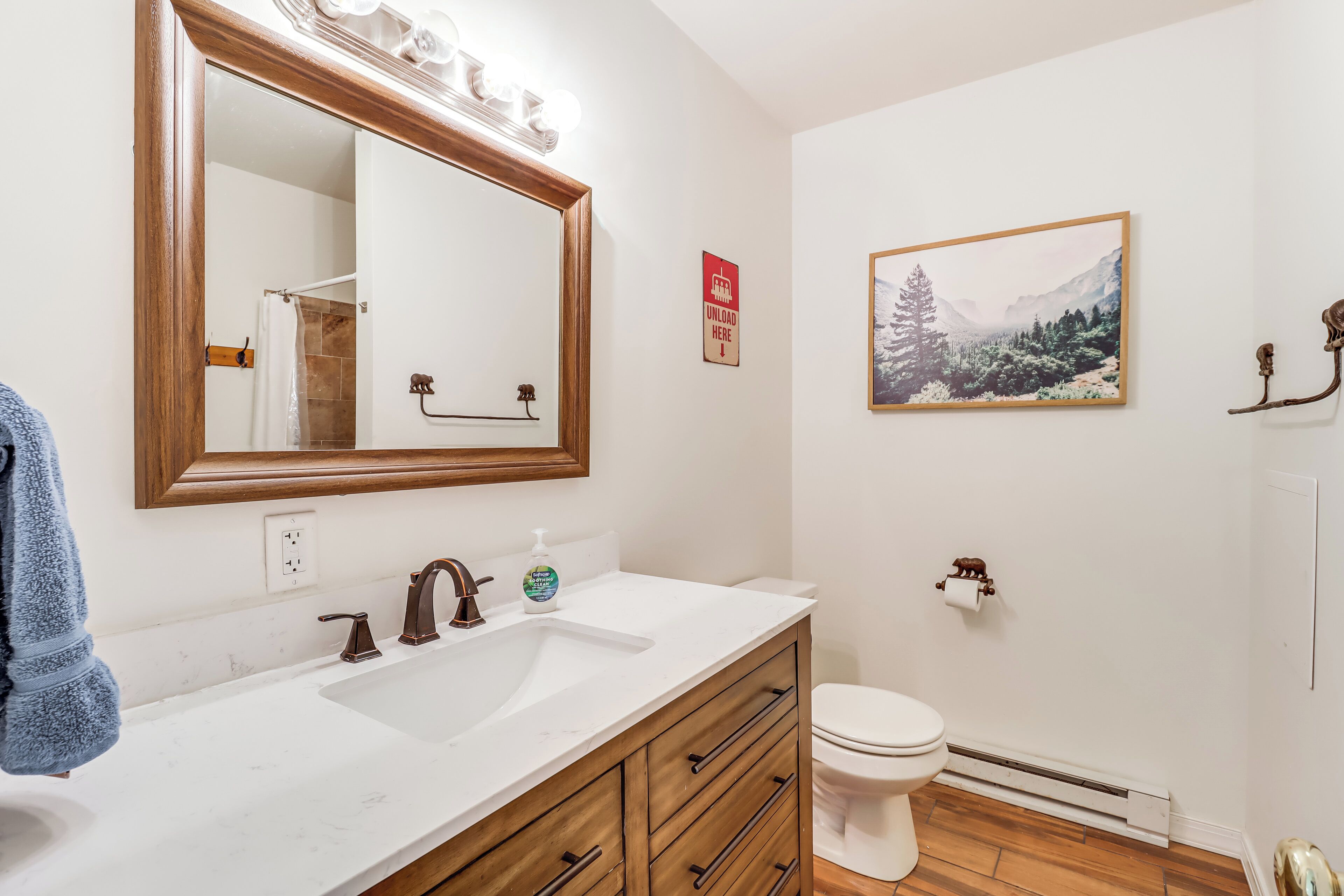 A bathroom with a wooden vanity, a large mirror, a sink, a toilet, and a framed picture on the wall.