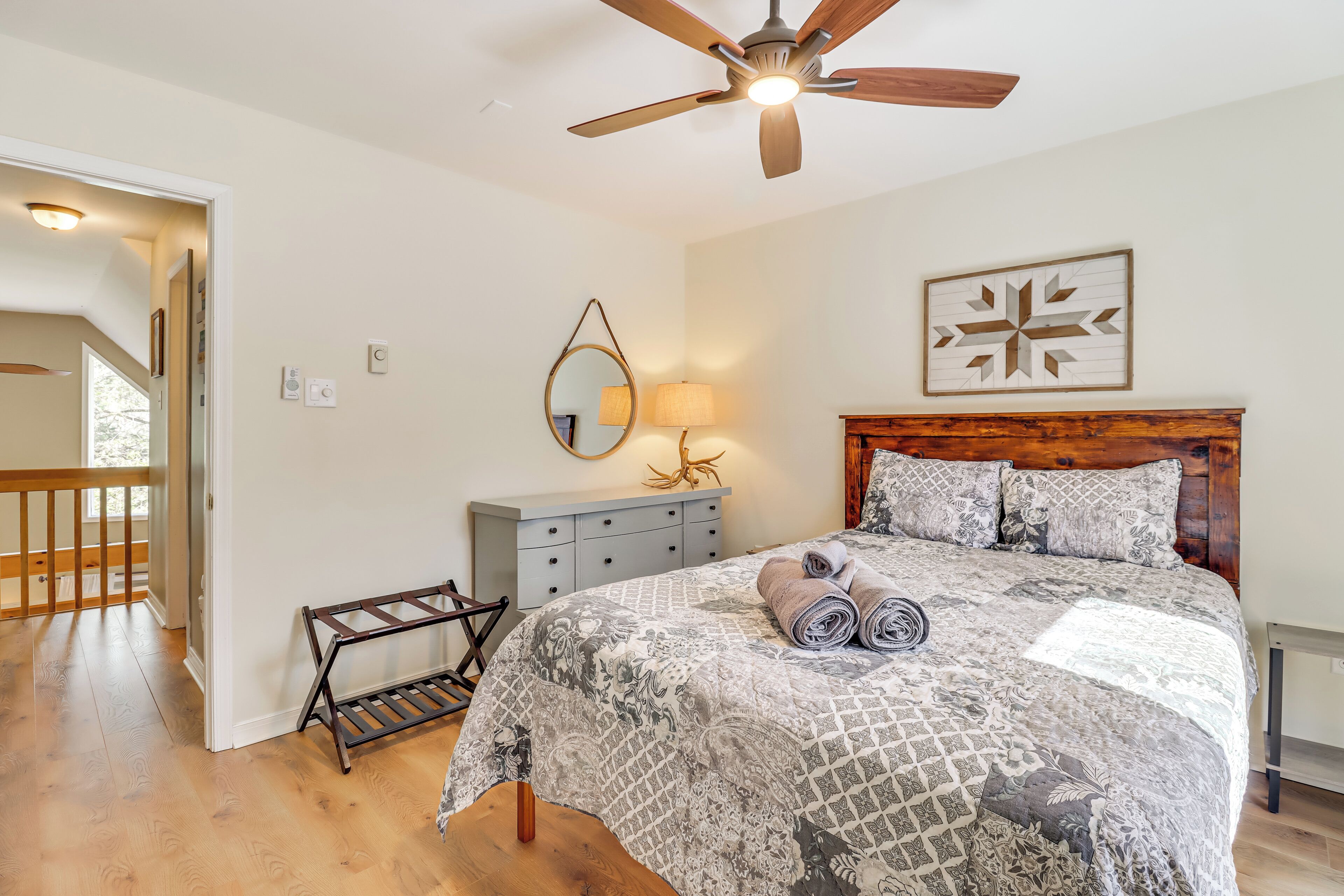 A bedroom with a bed, a ceiling fan, a bedside table with a lamp, and a wooden headboard.