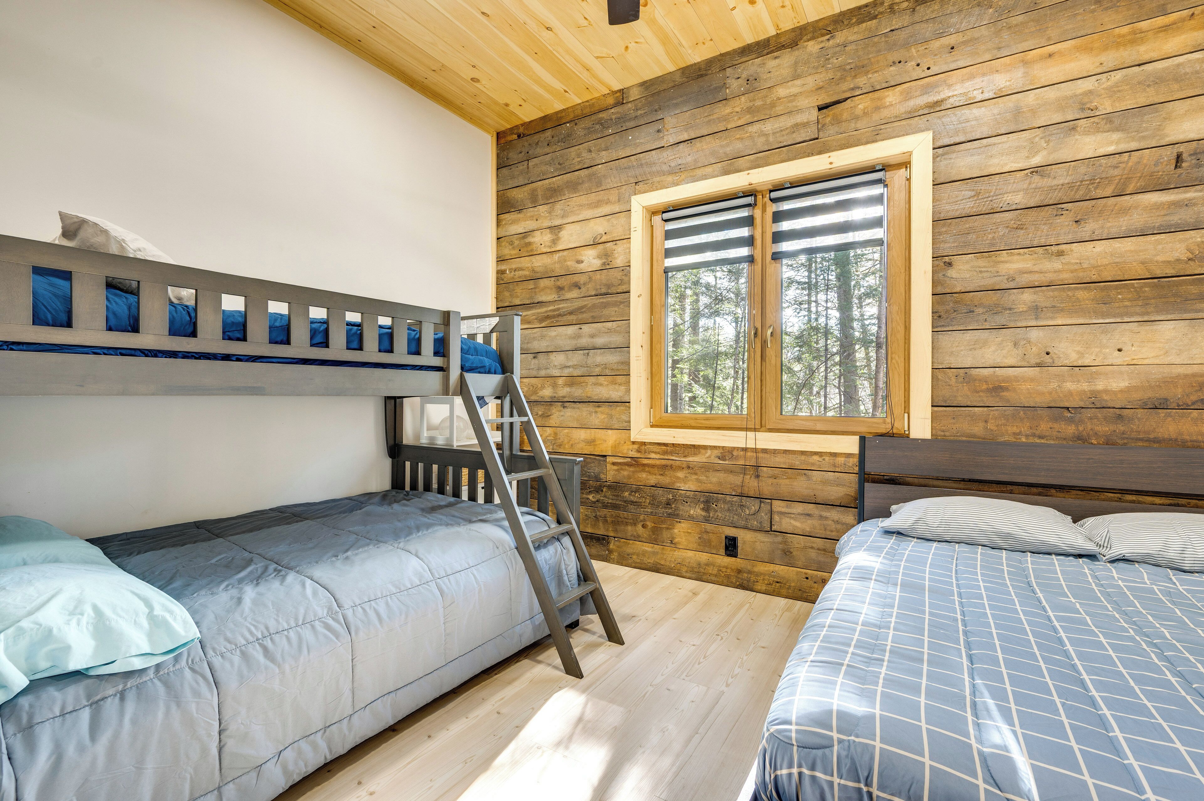 A cabin with two bunk beds, a ladder, and a window with a view of trees.
