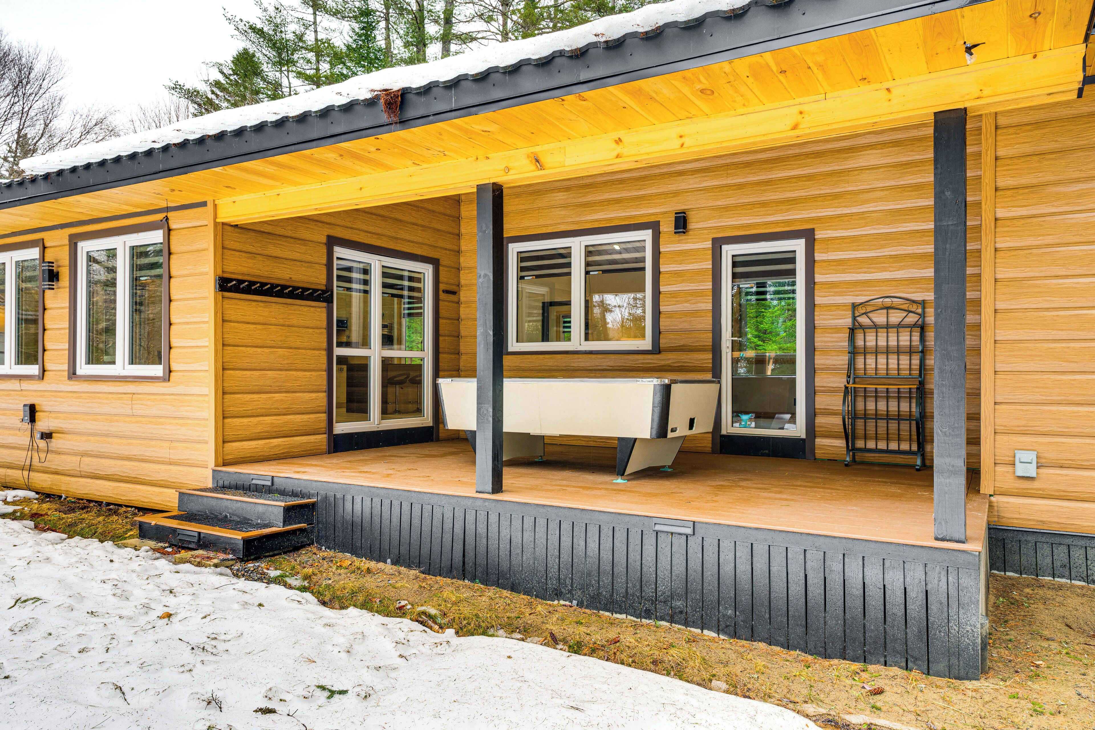 A wooden cabin with a covered porch, large windows, and a pool table.