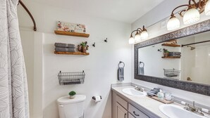 A bathroom with a toilet, two sinks, a large mirror, and decorative shelves.