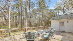 A wooden deck with outdoor furniture, surrounded by tall trees.