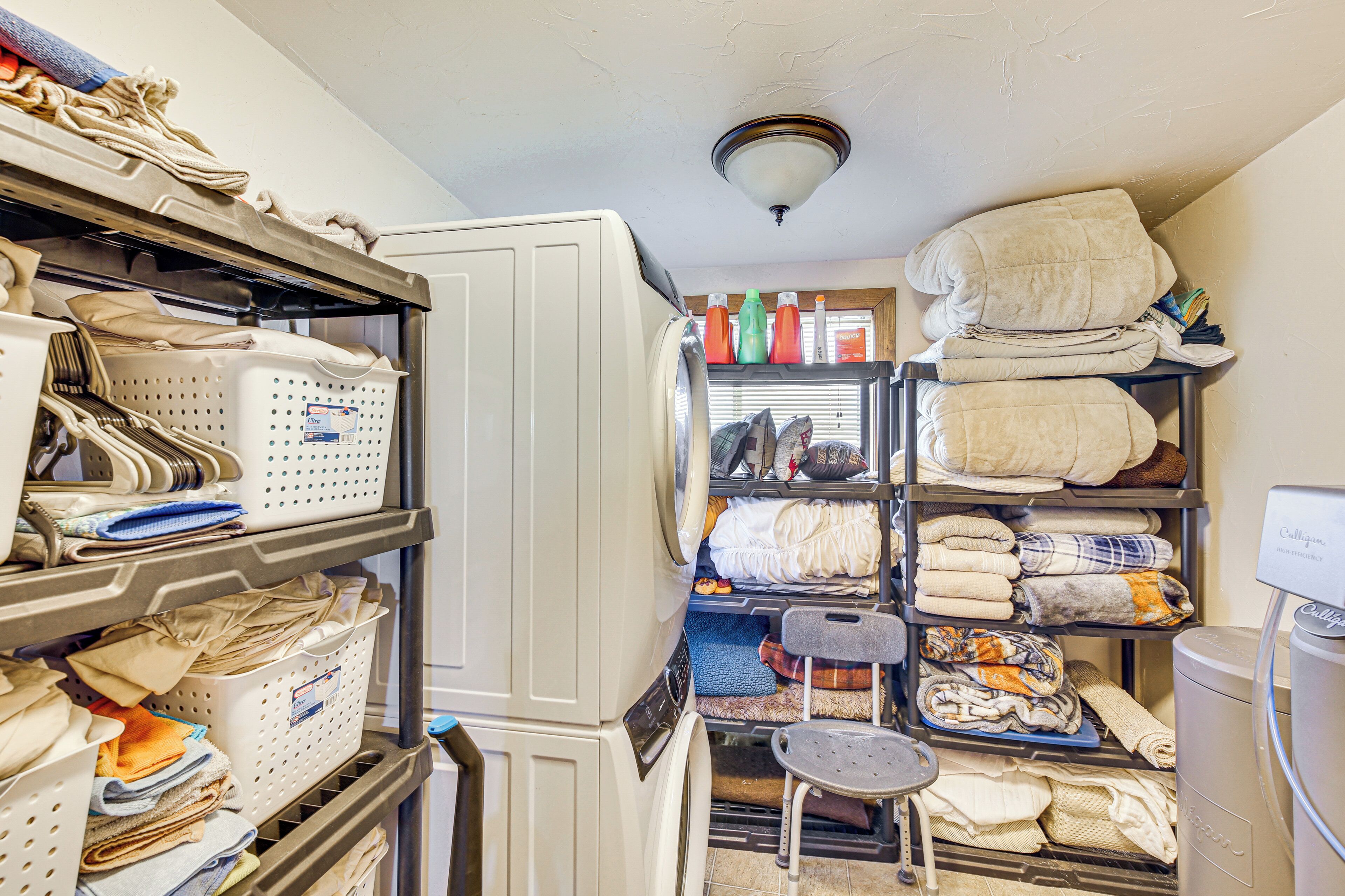 A laundry room with shelves of folded clothes, a washing machine, and a drying rack.