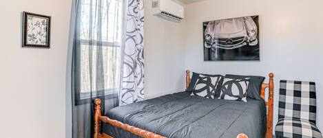 A bedroom with a wooden bed, a checkered chair, a wall-mounted air conditioner, and a car-themed artwork.