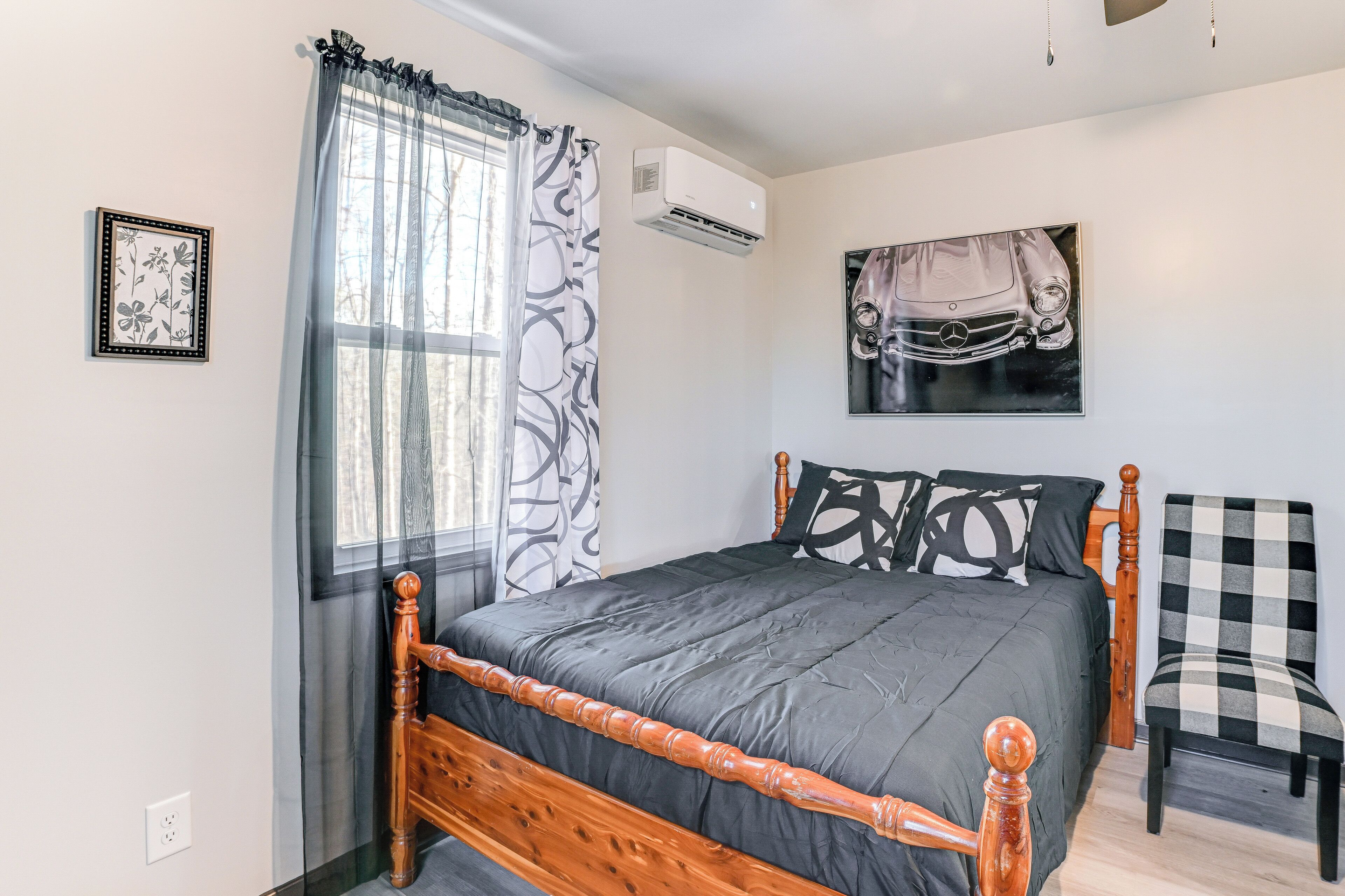 A bedroom with a wooden bed, a checkered chair, a wall-mounted air conditioner, and a car-themed artwork.