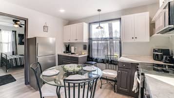 A modern kitchen with a glass dining table, stainless steel appliances, and a large window.