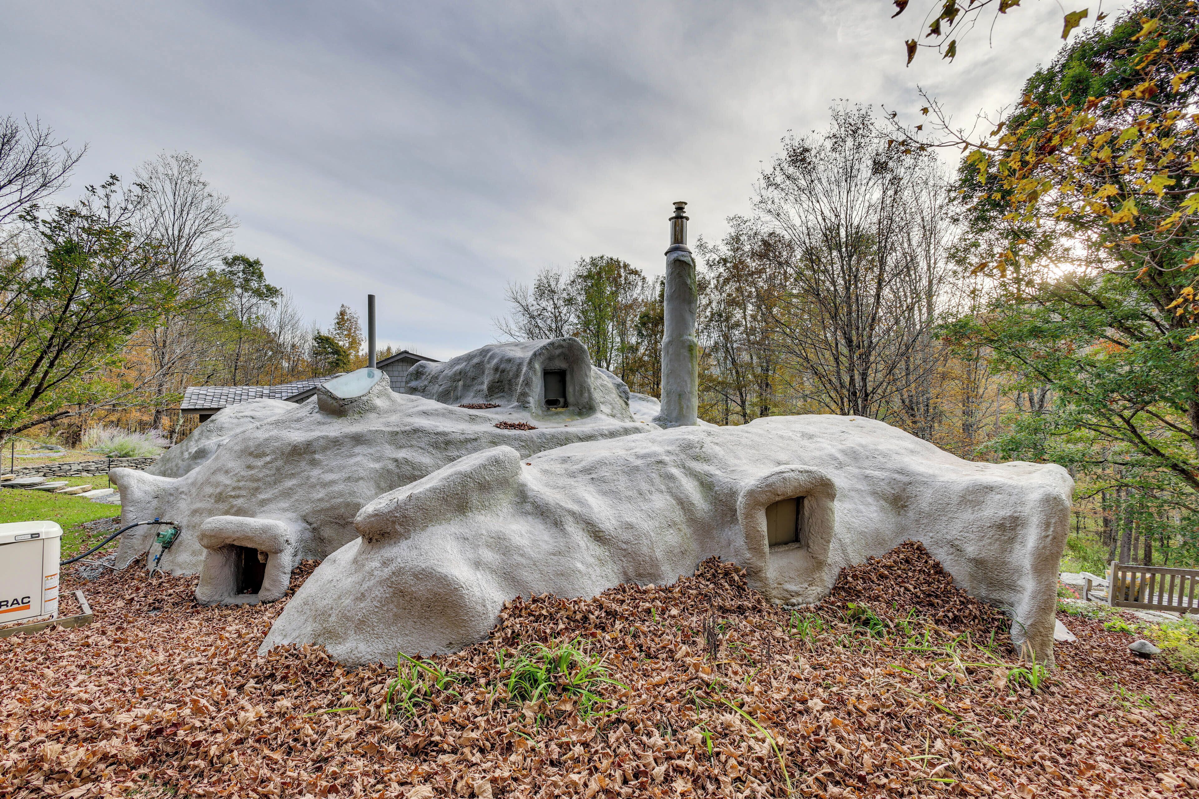 A stone structure resembling a cave with a chimney, surrounded by trees and fallen leaves.