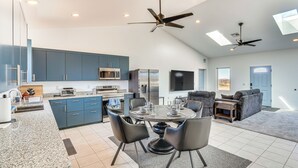 A modern kitchen with blue cabinets, a dining area with a round table and chairs, and two ceiling fans.