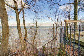 Un escalier en bois mène à une plateforme dotée d’une rambarde en métal, qui est entourée d’arbres et offre une vue sur une étendue d’eau.