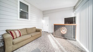 A living room with a beige sofa, a striped pillow, a flat-screen TV on a wooden stand, and a patterned rug.