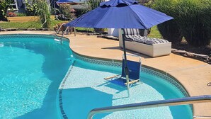 En swimmingpool med ett blått parasoll, solstolar och en kakelbeklädd terrass.