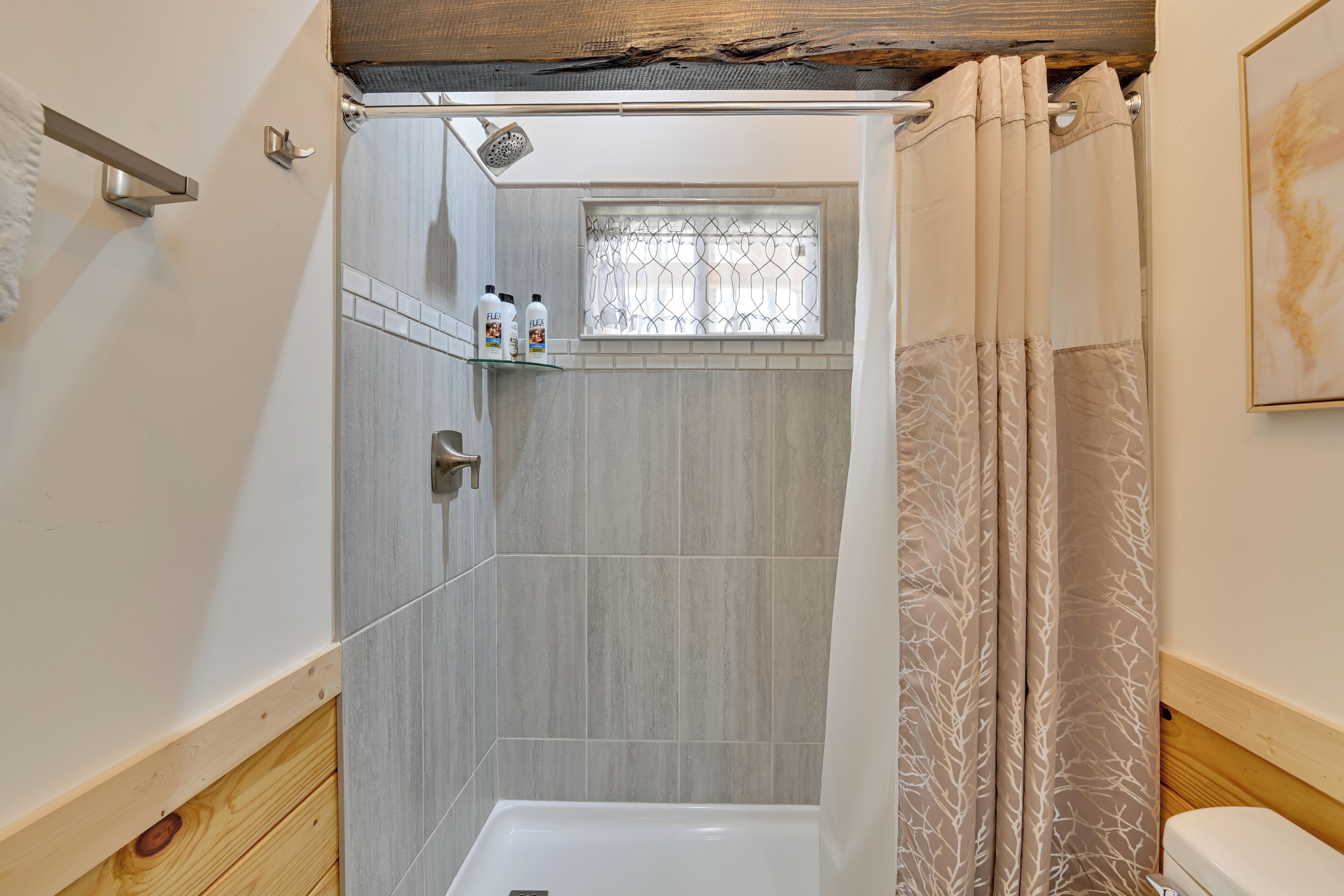 Une salle de bain avec une douche, des toilettes et une fenêtre dotée d’une grille métallique.