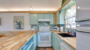 A kitchen with light blue cabinets, a wooden countertop, a white stove, a microwave, and a sink.