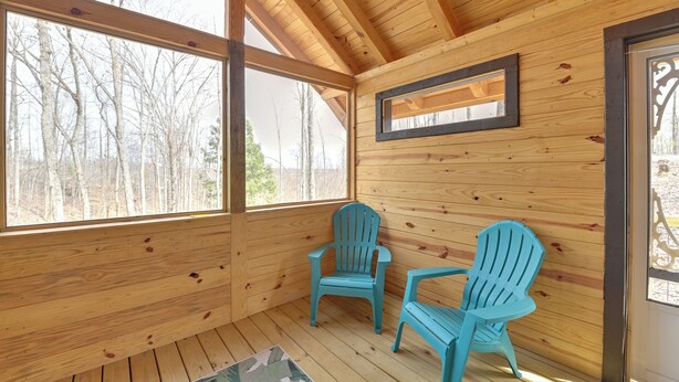Une cabane en bois avec deux chaises Adirondack bleues, de grandes fenêtres et un miroir encadré accroché au mur.