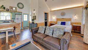 Une pièce spacieuse avec un ventilateur de plafond en bois, un lit doté d’une tête de lit en bois et un canapé en cuir marron agrémenté de coussins à motifs.