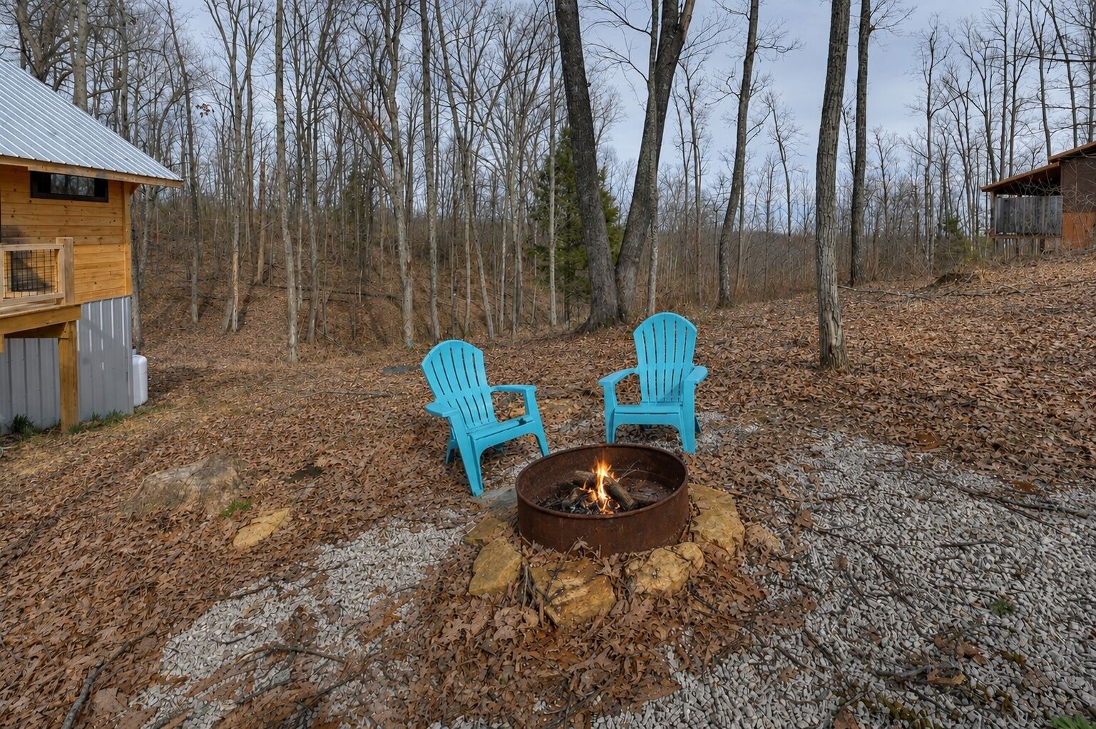 Una cabaña rústica con dos sillas Adirondack alrededor de una fogata.