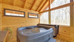 Une cabane en bois dotée d’un bain à remous, de murs en bois et de grandes fenêtres.