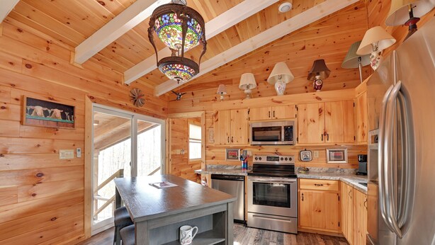 A wooden cabin interior with a kitchen featuring a stove, microwave, and refrigerator. - Plum Crazy: Frenchburg Cabin on 1 Acre (Frenchburg)