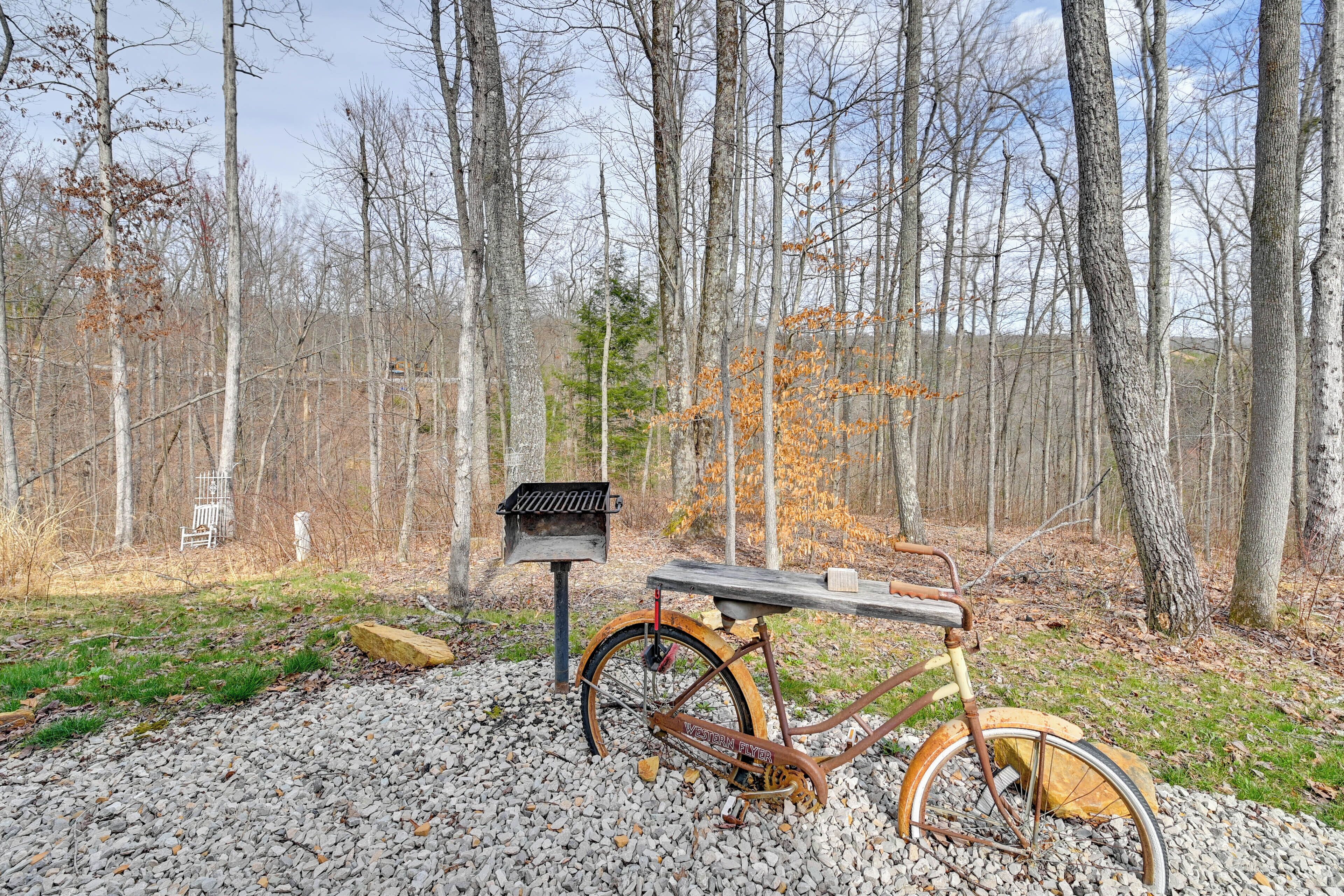 A rustic wooden bench with a metal frame, a vintage bicycle, and a metal bird feeder in a forested area.