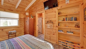 A cozy wooden room with a bed, a television, a bookshelf, and a window. - Plum Crazy: Frenchburg Cabin on 1 Acre (Frenchburg)