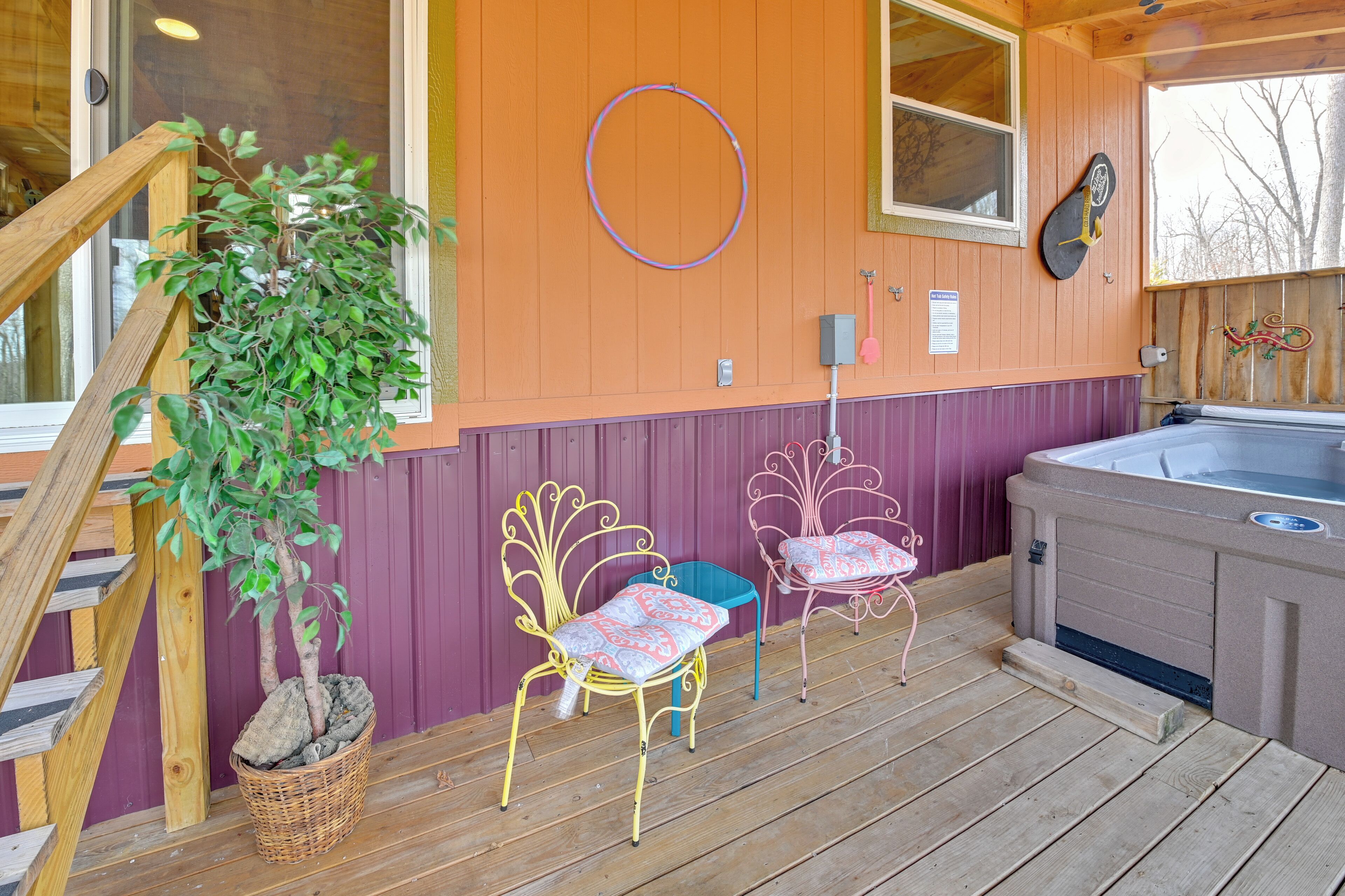 A wooden deck with two metal chairs, a hot tub, and a potted plant.