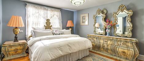 A bedroom with a bed, two nightstands, a dresser, a chandelier, and a patterned rug.