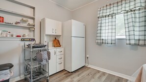 A compact kitchen with white cabinets, a white refrigerator, a metal cart with kitchen items, and a window with plaid curtains. - Boat, Hike, & Golf: Inviting Inverness Getaway! (Inverness)