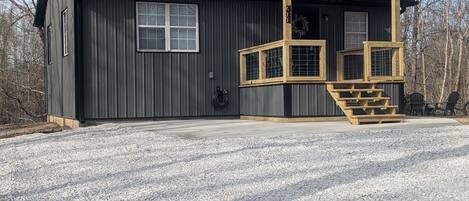 A two-story building with a dark exterior, a wooden deck, and a gravel driveway.