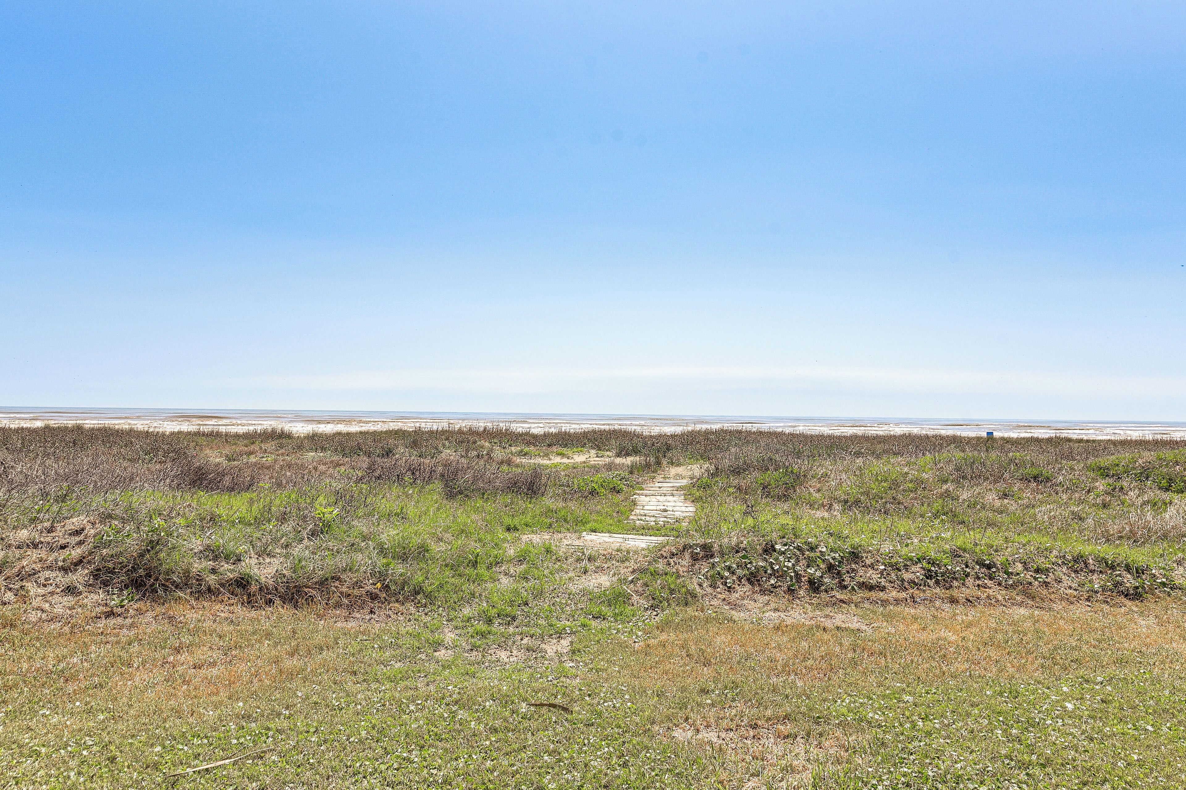 A pathway leading through a natural landscape with sparse vegetation and a clear sky.