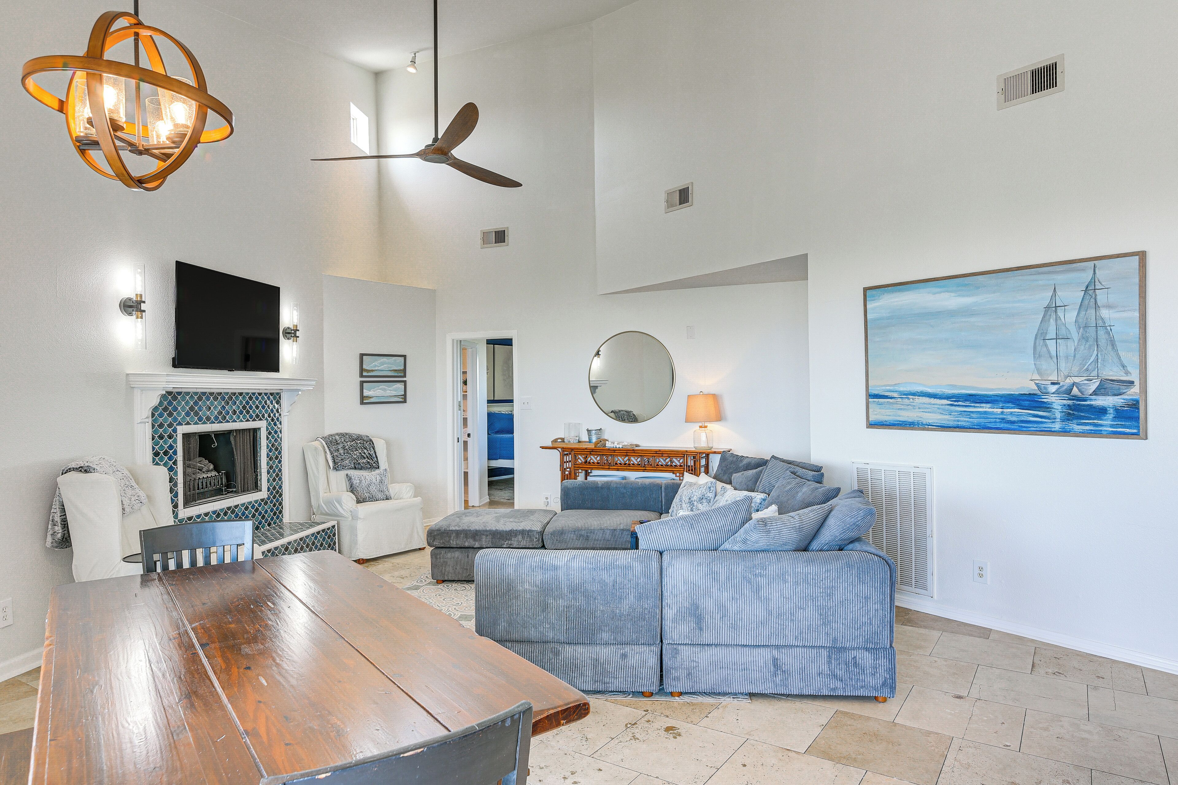 A spacious living room with a wooden dining table, a grey sofa, a white armchair, and a fireplace.