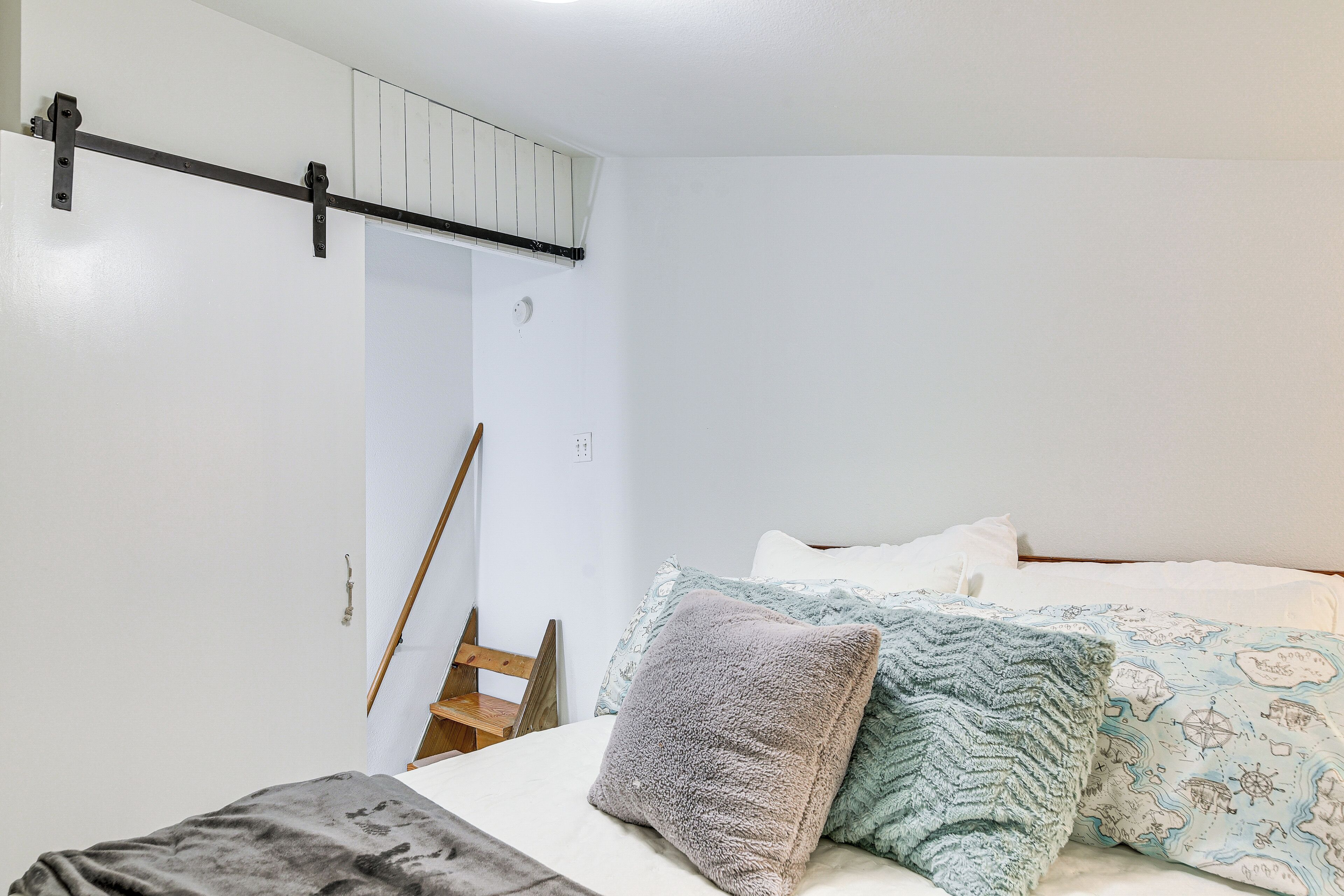 A bedroom with a bed, pillows, a wooden chair, and a white wall.