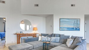 Ein Wohnzimmer mit einer Eckcouch, einem runden Spiegel, einem Kamin und einem Gemälde eines Segelbootes.