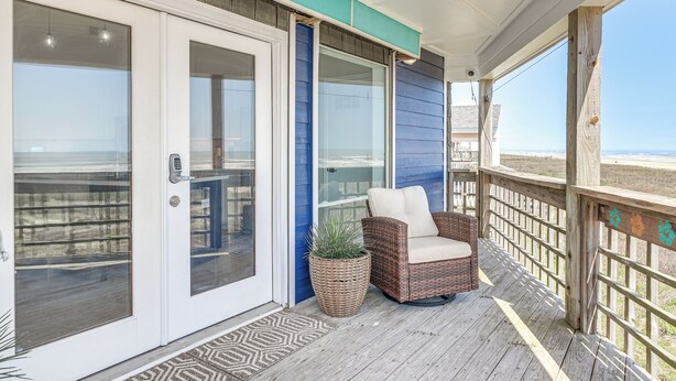 Eine überdachte Veranda mit einem Korbstuhl, einem Blumentopf und Blick auf den Strand.