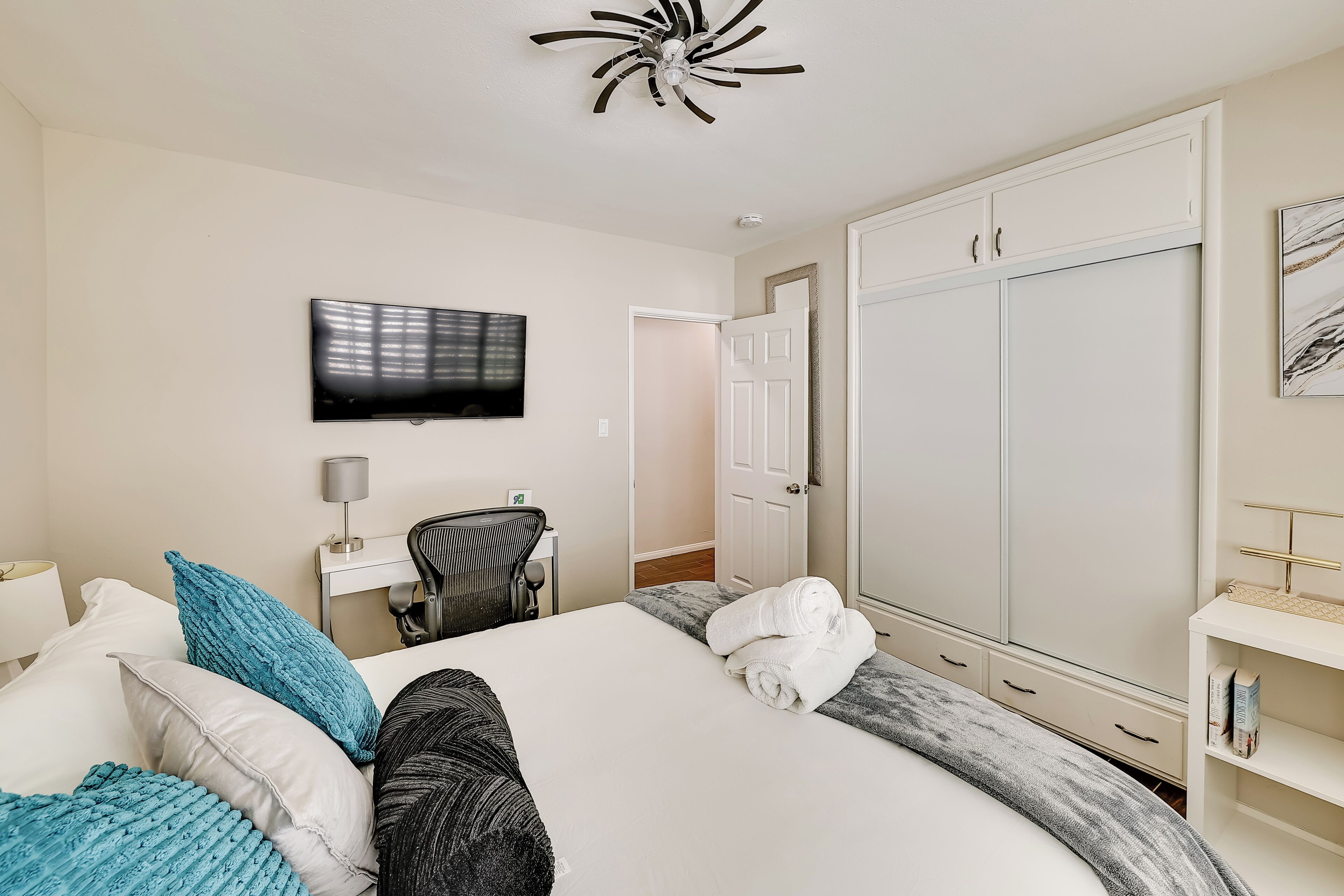 Habitación de hotel con cama, televisor montado en la pared, armario y escritorio con silla.