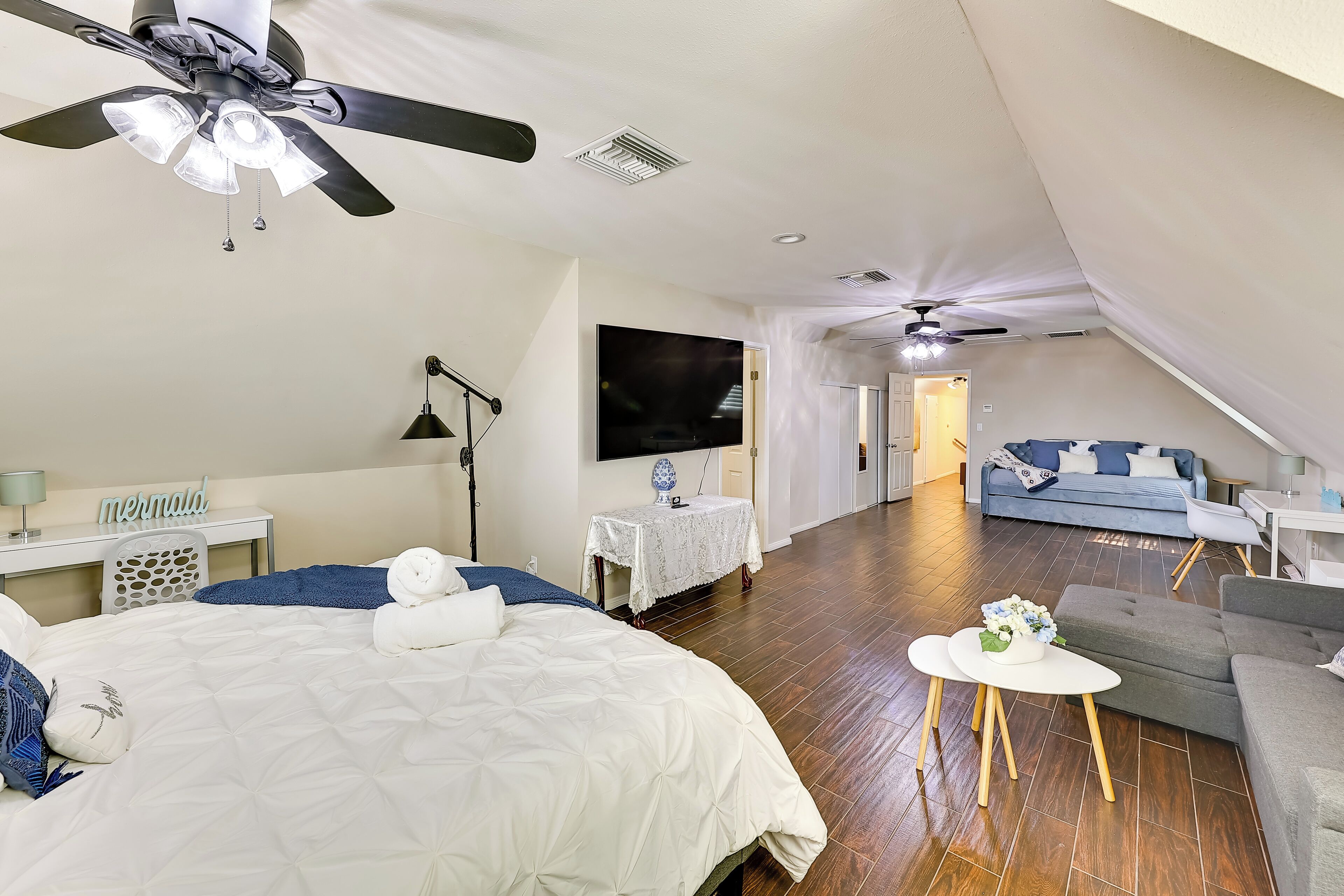 Quarto com cama, escrivaninha, televisão e ventilador de teto.