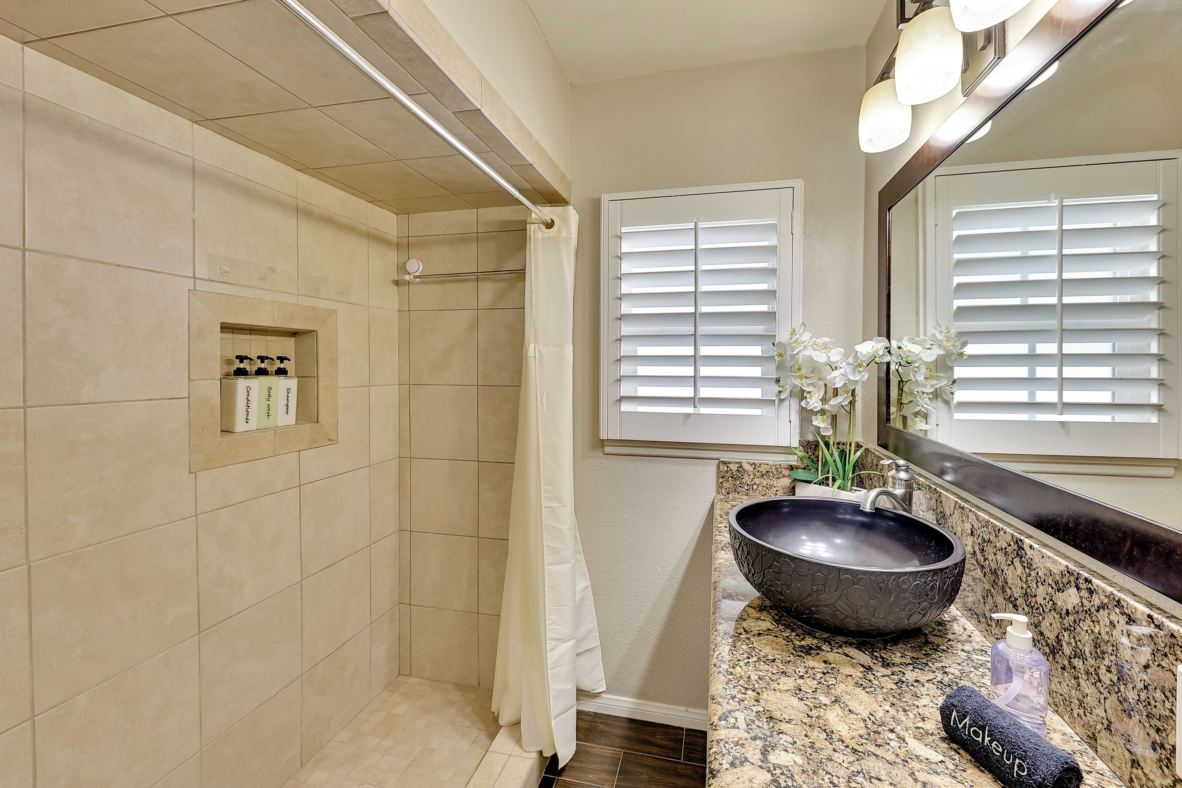 A bathroom with a walk-in shower, a vanity with a large bowl sink, and a mirror with lights.